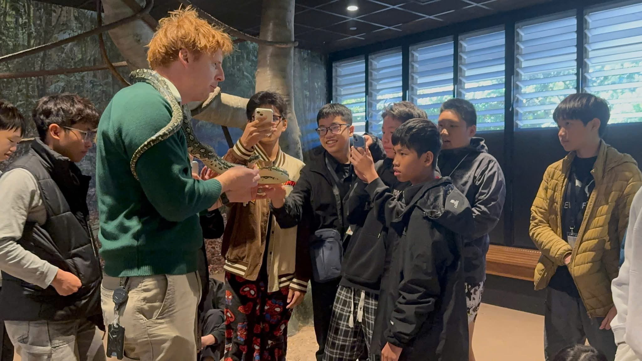 A wildlife guide showing a python to study tour students indoors